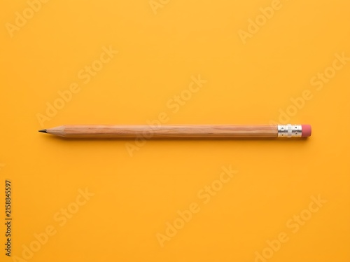 Single wooden pencil lying horizontally on a bright orange background
