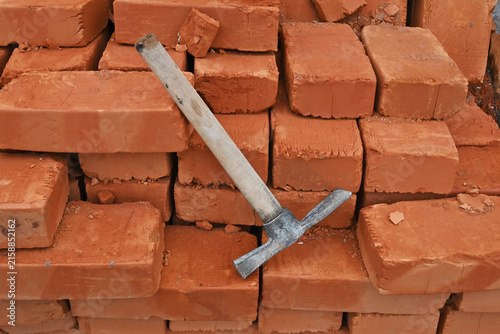 Obraz na płótnie A construction hammer resting on a stack of rough red bricks at a construction site