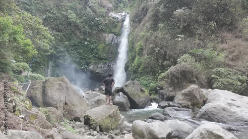 Man Standing Beside a Waterfall in a Tropical Forest