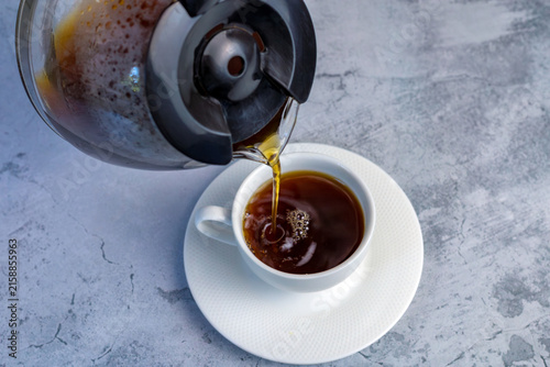 Принти на полотні Fresh brewed coffee is being poured into a white cup from a glass carafe