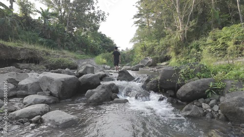 Man Walking Across a Rocky Stream in a Tropical Forest