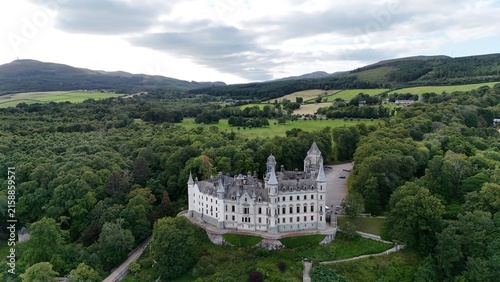 High angle aerial shot of Dunrobin Castle, historic Scottish Baronial estate surrounded by coastal forest in Sutherland