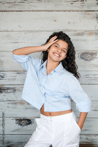 Playful Teenage Girl Touching Curly Hair Against Rustic Wall Background