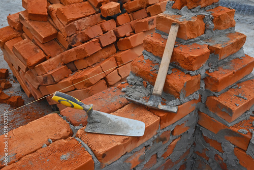 Cuadro en lienzo A trowel and a hammer lie on an unfinished wall, symbolizing construction work and the process of erecting a brick structure