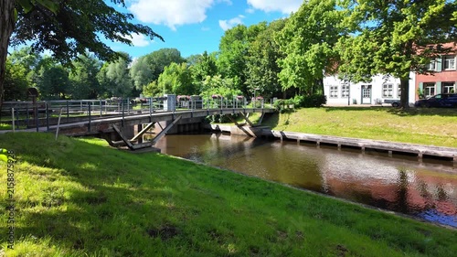 Small bridge over an idyllic canal with green banks and historic houses in Friedrichstadt. Historic houses,waterways and lush greenery combine traditional urban architecture with a natural environment