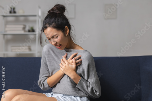 Foto Woman holding chest in pain while sitting on sofa at home, showing sudden discomfort, heart health concern, chest pressure, illness symptoms, medical emergency, healthcare and wellness concept
