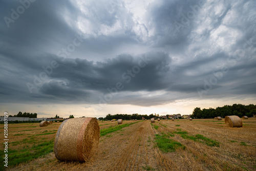 Dramatic sky over harvested field with round hay bales before storm arrival in the Po Valley, northern Italy