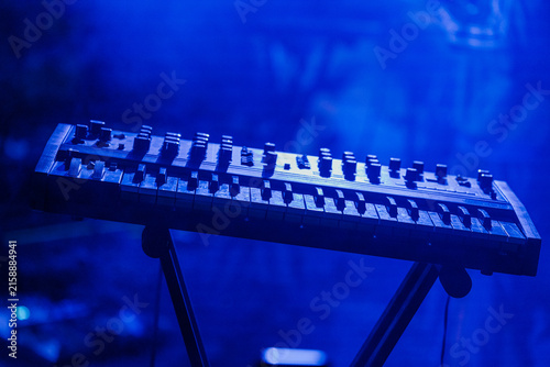 Foto Electronic keyboard synthesizer on a stand illuminated by intense blue concert l