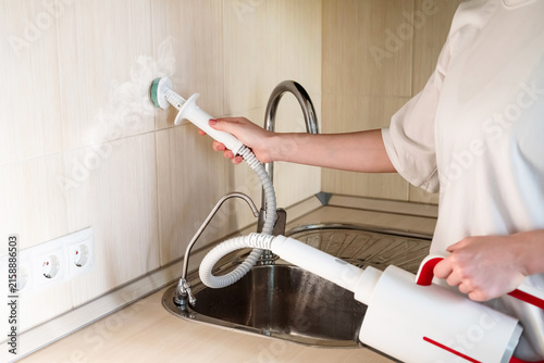 Cleaning the kitchen surface with a steam cleaner next to the sink at home
