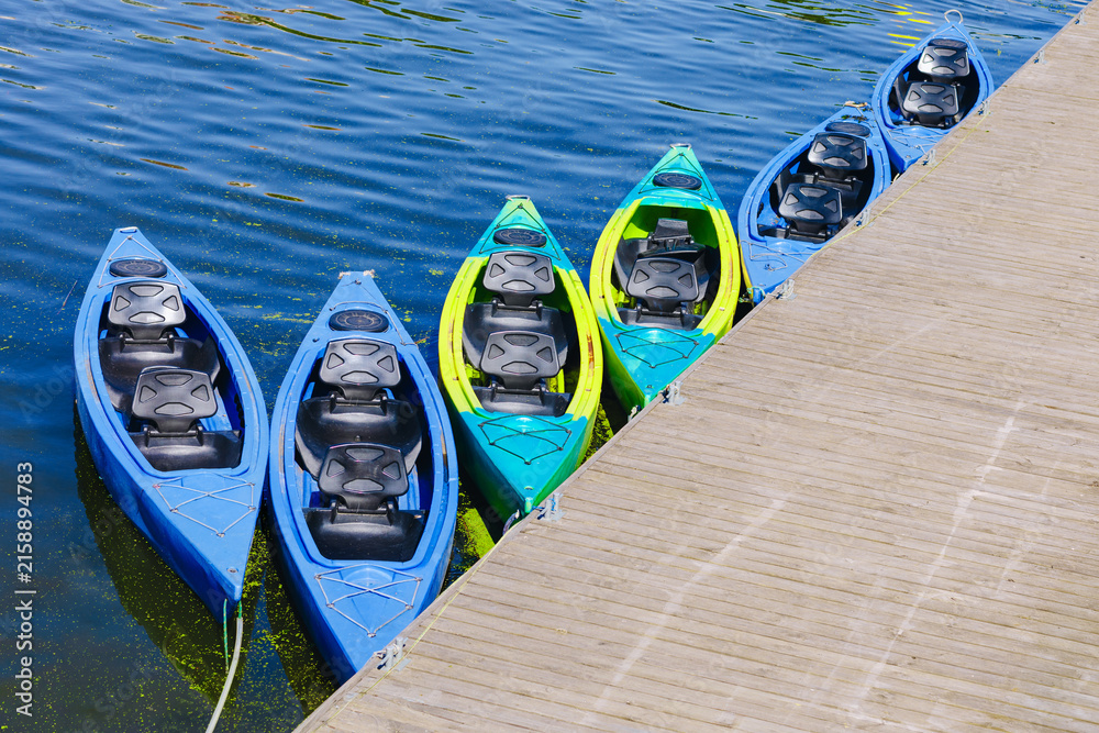 Fototapeta premium Colorful Tandem Kayaks Moored Beside a Wooden Dock on a Calm Lake