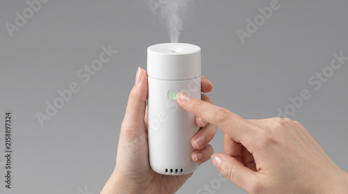 小型の超音波加湿器を手で持ち電源スイッチを押す女性の操作風景