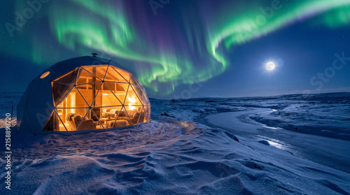A glowing geodesic glass dome sits in a snowy landscape with green northern lights and a full moon over a frozen river at night.