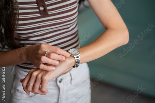 Принти на полотні A woman sits and looks at her watch while in a relaxed indoor space