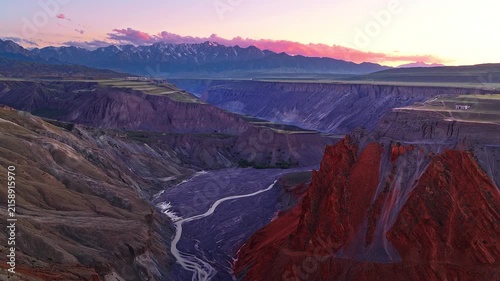 Aerial view of a deep gorge with a winding river and red cliffs at sunset in Anjihai Grand Canyon, Xinjiang, China