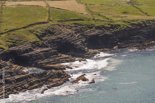 Rugged cliffs meet crashing waves beneath a bright sky