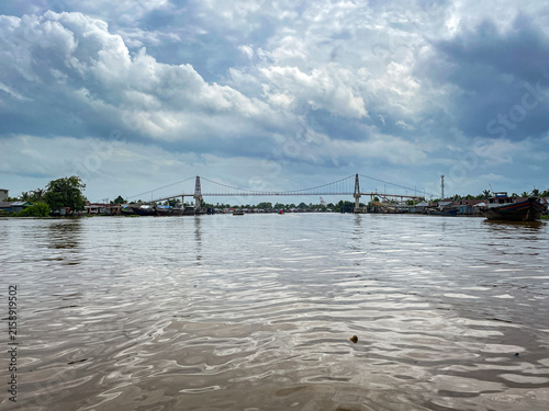 Photography Wide suspension bridge spans murky river under cloudy sky