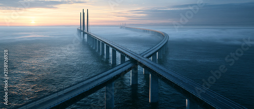 Bridge ocean sunrise fog highway coastline global economic outlook across curved sea crossing with tall pylon and calm water under pastel sky near distant horizon