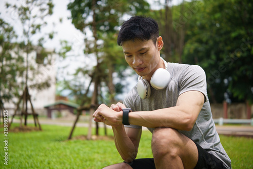 Young Asian athlete checking a smartwatch while resting after exercise.