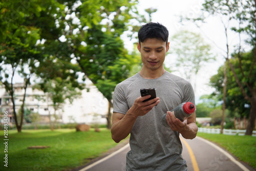 Young Asian athlete checking a smartphone while holding a water bottle.