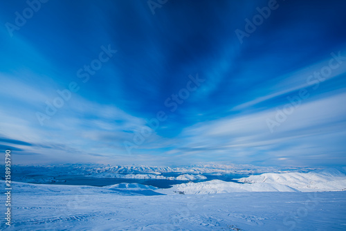Panoramic winter scenery of Yamdrok Lake surrounded by snow-covered mountains after fresh snowfall in Tibet Autonomous Region, China. The vivid turquoise-blue waters contrast beautifully with the whit