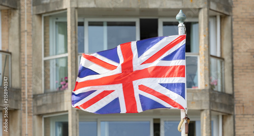 Union Jack Flag Waving On A Pole In Front Of Residential Building Exterior In The UK