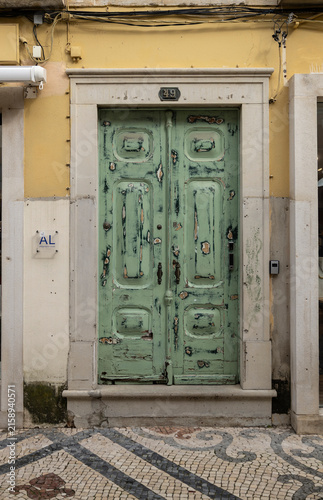 Weathered Green Door in Yellow Facade With Patterned Mosaic Pavement and Stone Frame