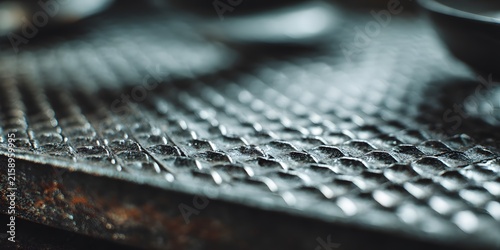 Closeup texture of a dark metallic surface with a repetitive pebblelike pattern and soft lighting.