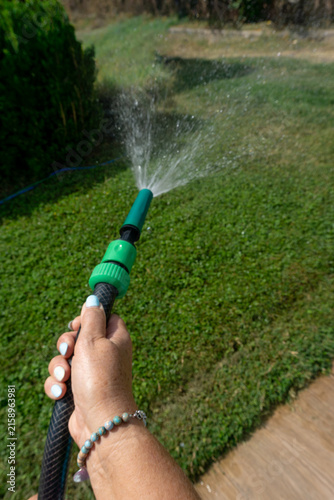 Vertical close up of hand holding garden hose nozzle spraying water on green lawn