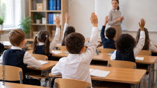 Élèves de l'école primaire levant la main en classe pour répondre à la question de l'enseignante.