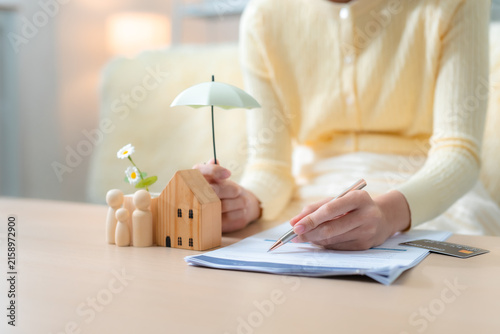 Fotografie Person reviewing home insurance documents with house model, family figures, umbrella, credit card, representing property protection, financial planning, coverage and family security