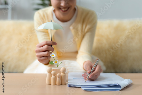 Fotografie Woman reviewing insurance documents with family figures under an umbrella, representing family protection, life insurance, financial security, coverage, planning, safety and future care