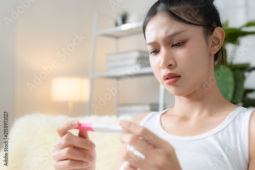 Foto Concerned young woman checking a pregnancy test at home, expressing anxiety and uncertainty about the result, reproductive health, fertility, family planning and possible pregnancy