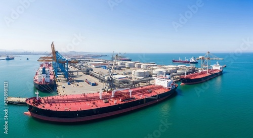 Massive petroleum tanker docked at an expansive industrial shipping terminal with cranes and storage tanks