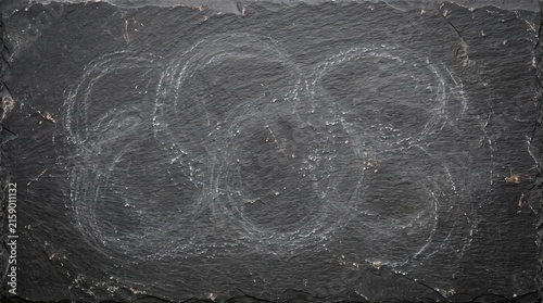 Dark natural slate stone background with abstract faint white chalk marks and textured surface