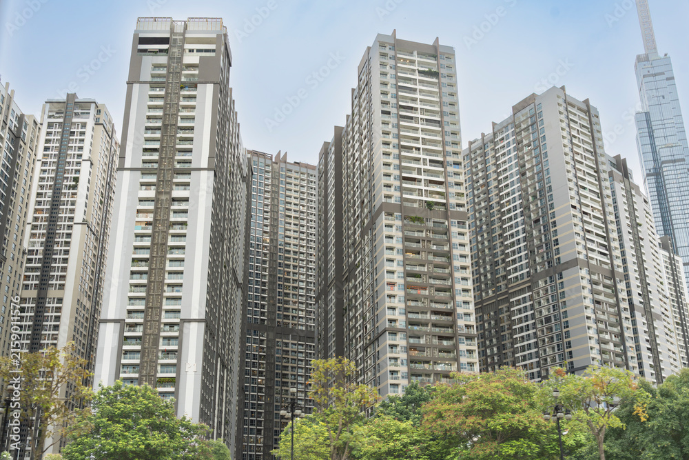 Fototapeta premium Modern high-rise residential apartment towers towering over green trees, with Landmark 81 visible in the background in Ho Chi Minh City, Vietnam.