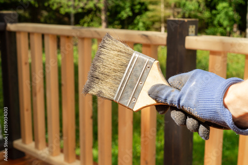 Quadro su tela Hand in protective glove painting a wooden deck railing with a brush outdoors