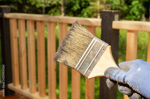 Cuadro en lienzo Hand in protective glove painting a wooden deck railing with a brush outdoors
