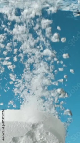 A fizzing tablet dissolving rapidly in clear blue water, creating ascending bubbles