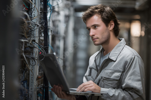 IT Technician Inspecting Server Rack With Laptop