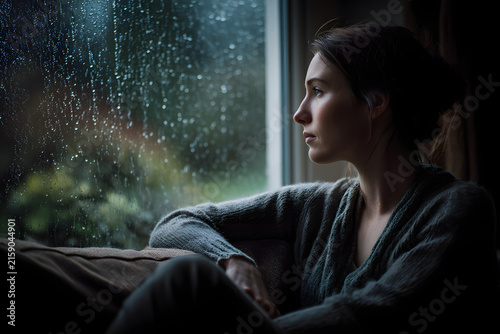 Woman sitting alone on couch looking out rainy window