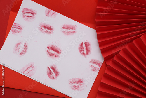 Lipstick kiss letter with red handmade paper fans on a red background. Valentine's Day.