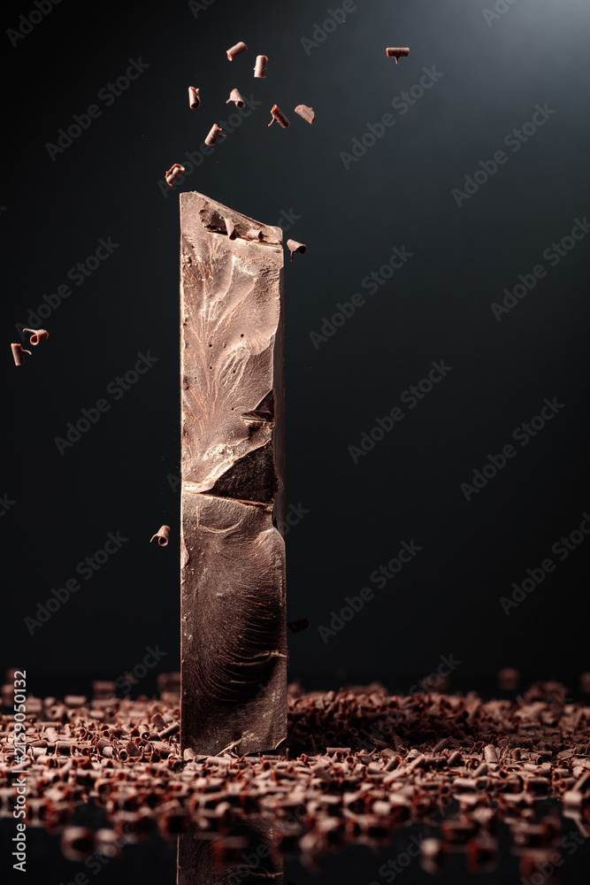 Naklejka premium Large piece of dark chocolate and falling chocolate crumbs.