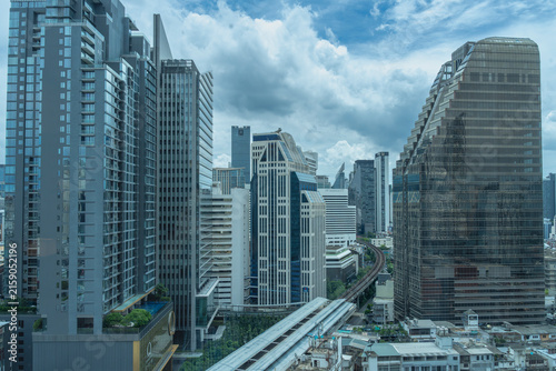 фотографія Modern Bangkok cityscape view featuring glass skyscrapers, a elevated BTS Skytrain track and station, and cloudy blue sky