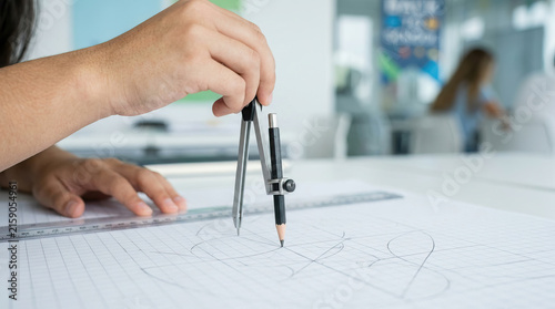 Student drawing geometric design with compass and pencil on drafting paper, showing focused creative study in bright classroom setting