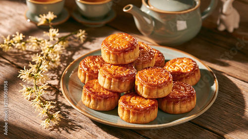 Warm morning light streaming across a rustic wooden table set for the Moon Festival. A stack of glossy baked mooncakes on a vintage celadon plate, a porcelain teapot with matching