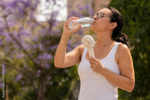 Woman Drinking Water and Cooling Off With Handheld Fan