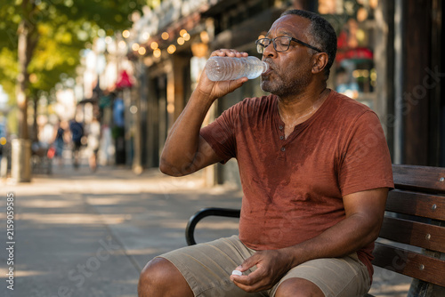 Sweaty Black Man Drinking Water on Bench During Heatwave