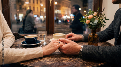 Two people gently holding hands across a cafe table during an intimate romantic moment