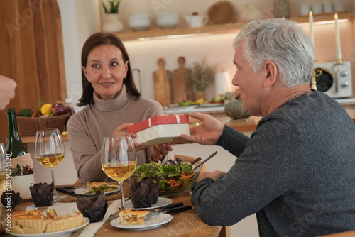 The elderly couple smiled happily. The grandfather held a gift box for the grandmother, who was surprised and delighted to receive the gifts as they celebrated Christmas and New Year with their family