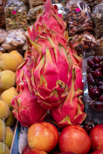 Bright pink dragon fruits stacked among other fruits and nuts at a colorful market stand in Guadalajara